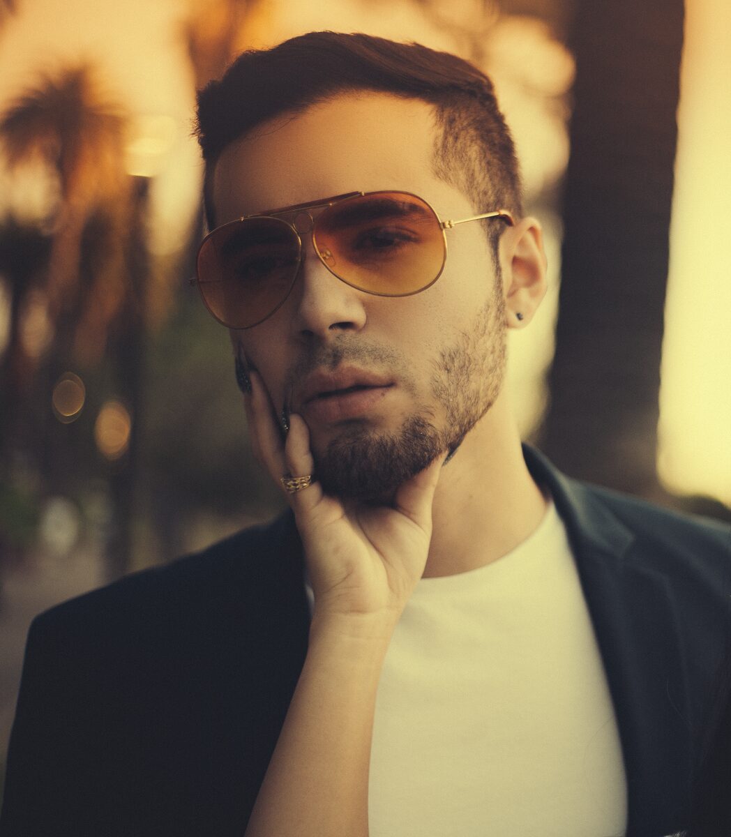 Portrait of a man in aviator sunglasses resting his chin on his hand, warm light behind him