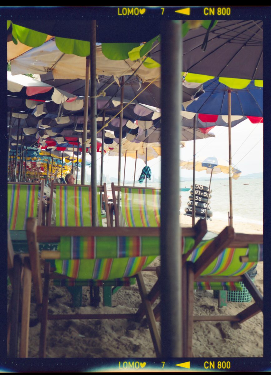 Film frame of beach umbrellas and striped deck chairs, with the film's edge markings visible