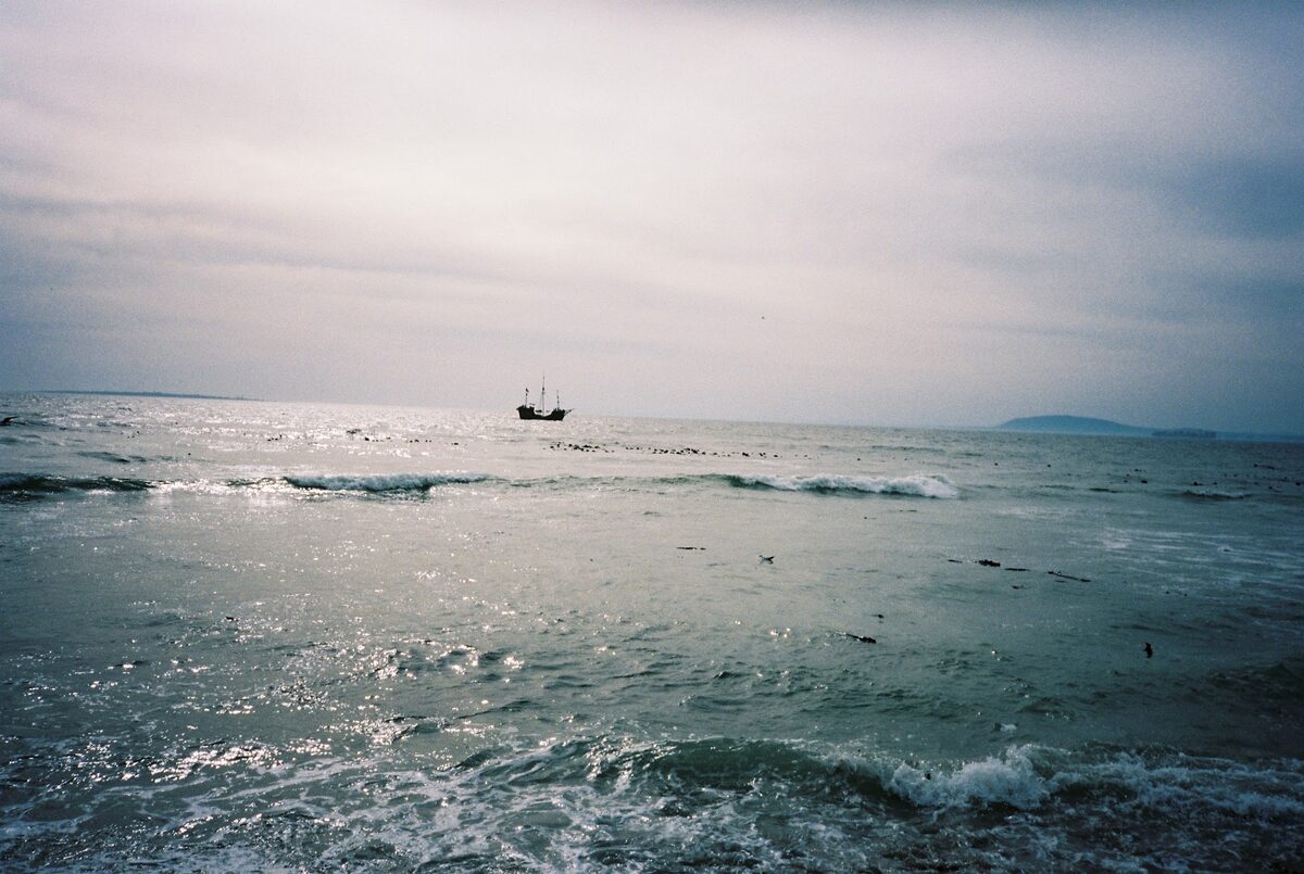A grey-blue sea under an overcast sky with a small ship on the horizon