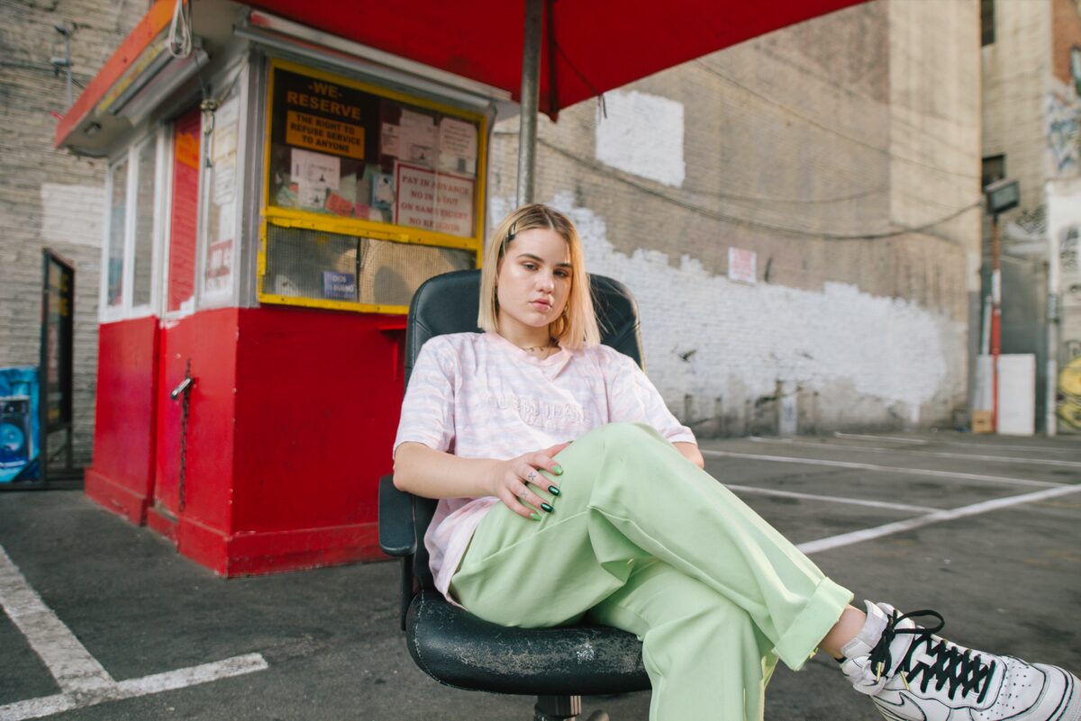 A woman in pale green trousers sitting in an office chair outside a small kiosk