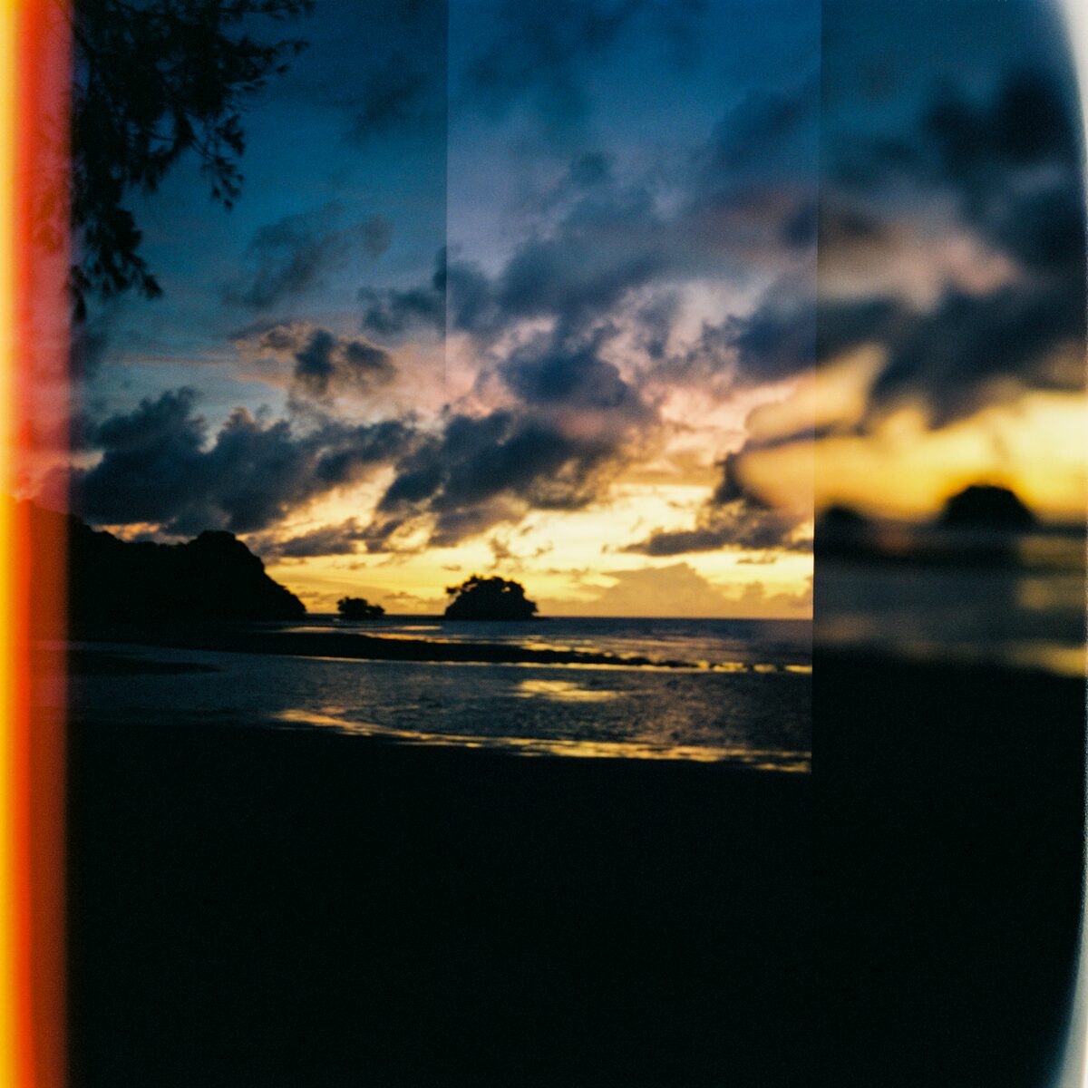 Sunset over the sea through heavy clouds, with an orange light leak along the left edge