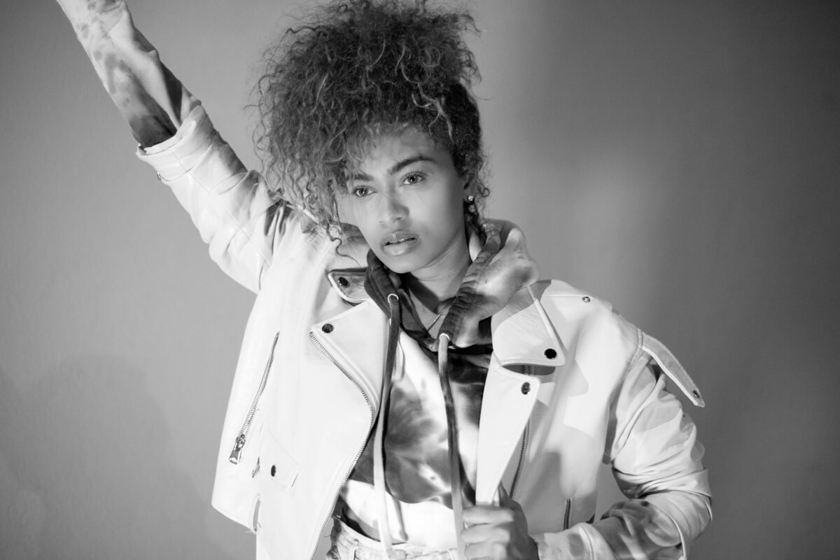 Black-and-white portrait of a woman in a white jacket with one arm raised